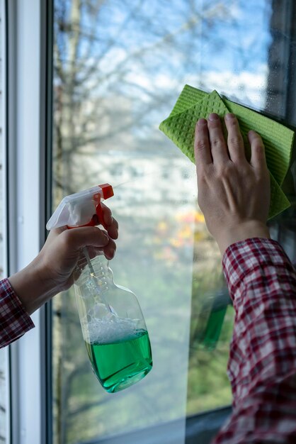 Le mani in una camicia a quadri fanno i lavori domestici e lavano la finestra con uno spray e una spugna