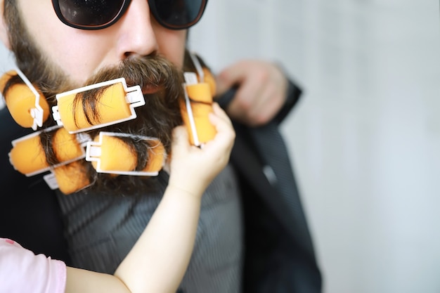 Le mani infantili del bambino afferrano la barba dell'uomo. Uomo allegro hipster con i bigodini in una barba.