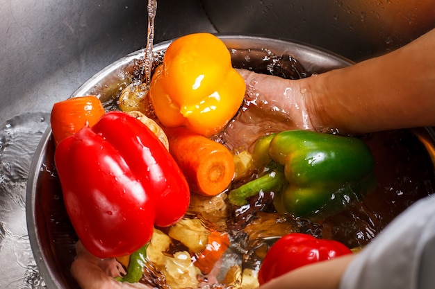 Le mani lavano le verdure nella bacinella. Paprica rossa e carota. Vivi una vita sana. Niente pesticidi o prodotti chimici.