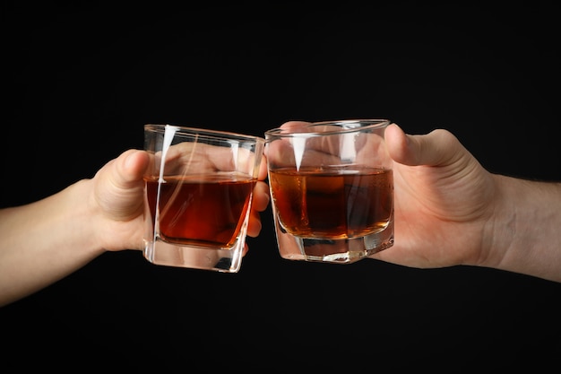 Le mani maschii tiene i vetri di whiskey su fondo nero, fine su. Saluti