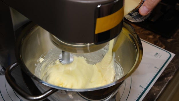 Le mani maschili aggiungono l'ingrediente latte condensato per la cottura nella ciotola di un robot da cucina