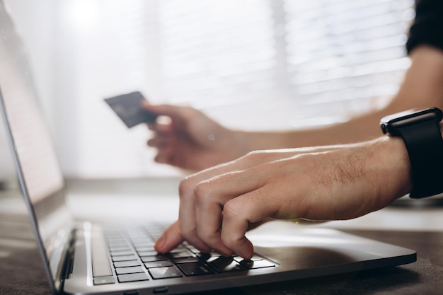 Le mani maschili del primo piano tengono una carta vicino allo shopping online del laptop