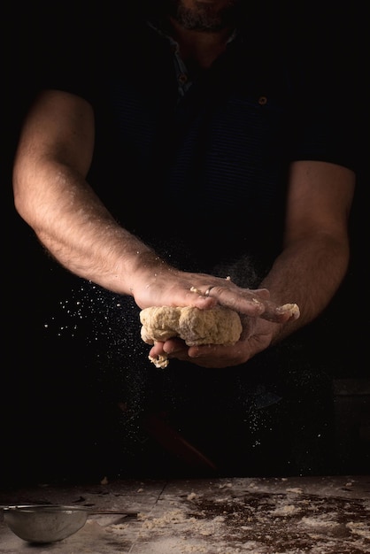 Le mani maschili stanno facendo la pasta su uno sfondo scuro