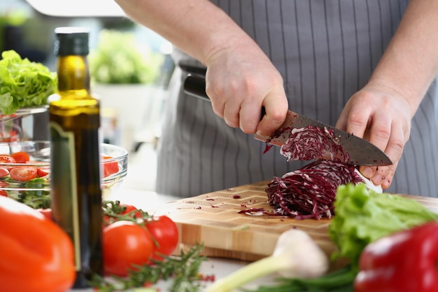 Le mani maschili stanno tagliando il cavolo rosso sul tagliere circondato da varie verdure fresche sul tavolo