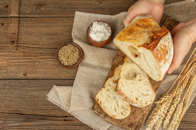 Le mani maschili tengono il pane appena sfornato. Frutti di mare, ciotole di farina e grano. Tavolo vintage con tavole di legno, prodotti da forno pronti, vista dall'alto