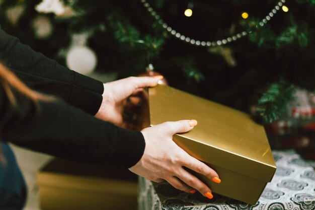 Le mani prendono il contenitore di regalo sotto l'albero di Natale