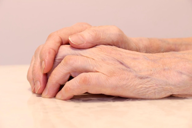 Le mani rugose della nonna piegate su uno sfondo bianco