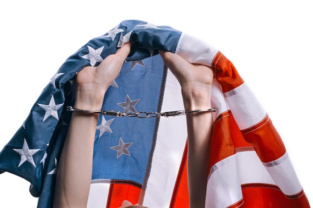 Le mani su uno sfondo bianco serrate a pugno con le manette allacciate su di esso le mani stringono la bandiera americana