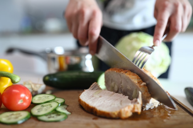 Le mani tagliano la carne suina e le verdure al forno pronte