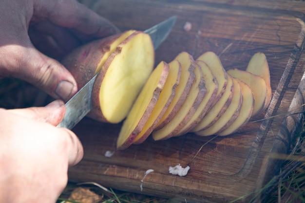 Le mani tagliano le patate per la griglia Cucinare il cibo in natura