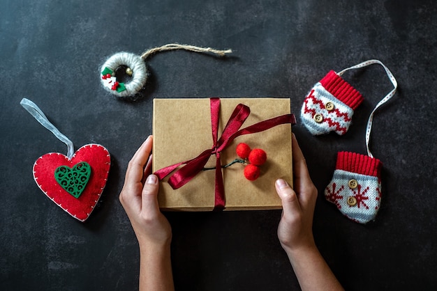 Le mani tengono il contenitore di regalo di Natale su backround scuro, contenitore di regalo di capodanno nelle mani del bambino, decorazione di Natale