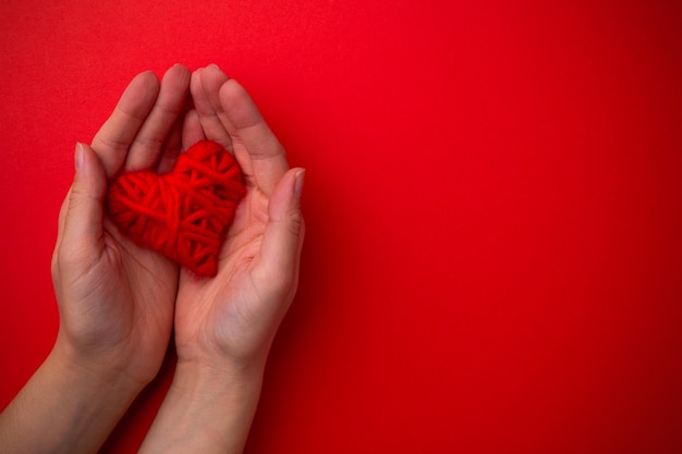 Le mani tengono il cuore rosso su sfondo rosso. Concetto di San Valentino