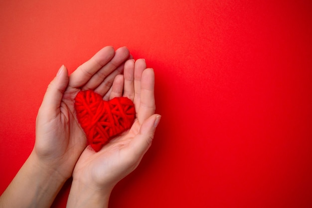 Le mani tengono il cuore rosso su sfondo rosso. Concetto di San Valentino