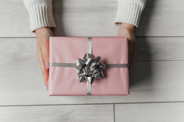 Le mani tengono il regalo di natale rosa su sfondo grigio isolato