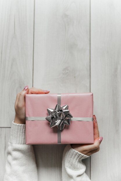 Le mani tengono il regalo di natale rosa su sfondo grigio isolato