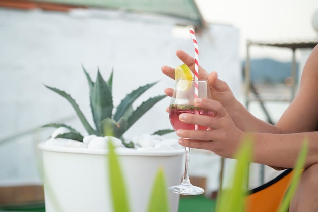 Le mani tengono un bicchiere con una bevanda fresca con una cannuccia al limone tra l'esterno con pla tropicale