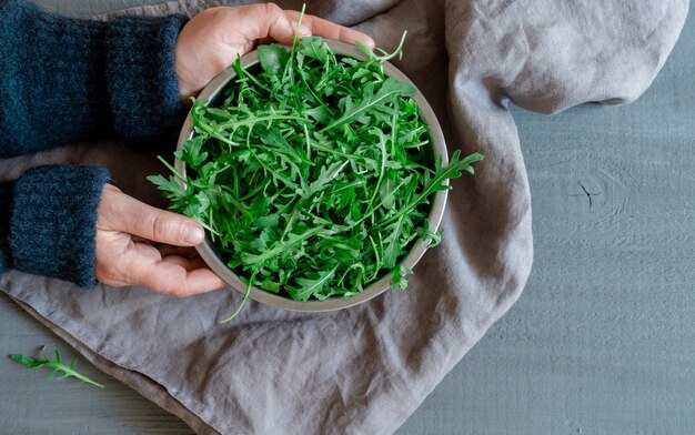 Le mani tengono un piatto con rucola fresca verde su sfondo grigio, concetto Tidewater Green Color.