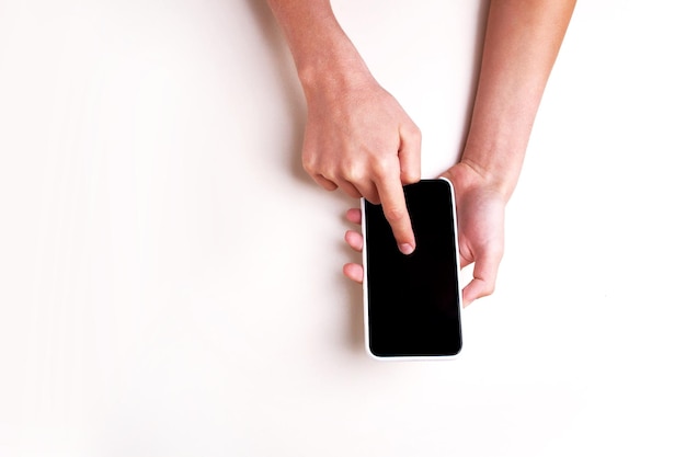 Le mani tengono un telefono su uno sfondo bianco isolato. Vista dall'alto