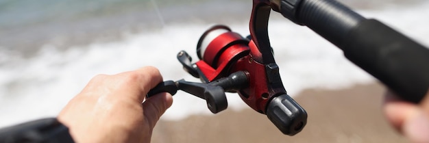 Le mani tengono una canna da pesca sullo sfondo della costa del mare