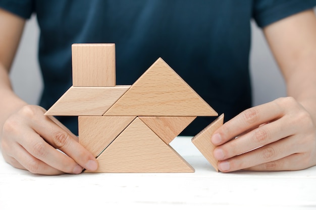 Le mani umane provano a costruire la casa o la casa con il puzzle di legno del tangram. Concetto di costruzione.