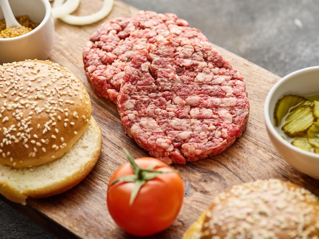 Le materie prime per l'hamburger fatto in casa Tortini di hamburger Carne tritata cruda cotoletta di manzo e maiale macinati con panino Sfondo grigio