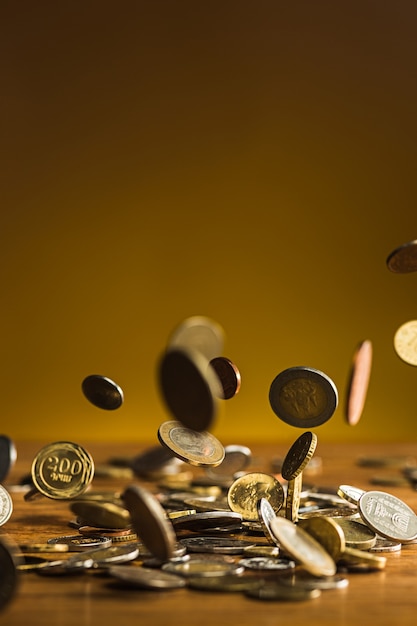 Le monete d'argento e d'oro e le monete che cadono su fondo di legno