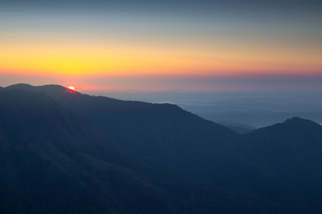 Le montagne osservano l&#39;orizzonte e le nuvole di alba arancio di fondo.