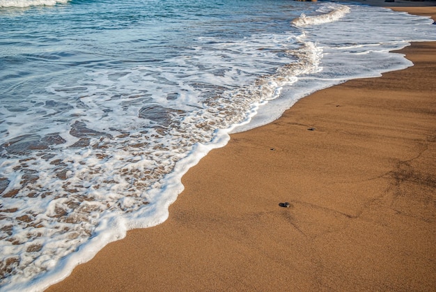 Le onde del mare con schiuma bianca corrono sulla sabbia Sfondo blu del mare