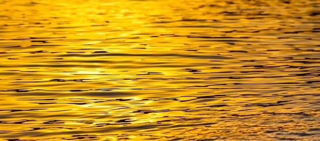 Le onde del mare dorate al tramonto brillano come sfondo della superficie Vacanze estive e concetto di natura costiera