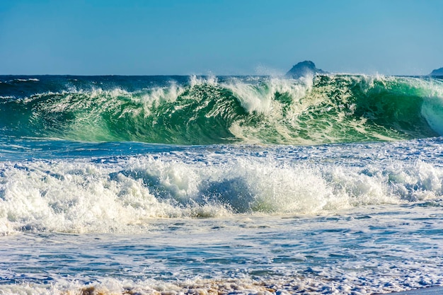 Le onde del mare si schiantano sulla spiaggia in estate con gocce d'acqua e schiuma che schizzano nell'aria