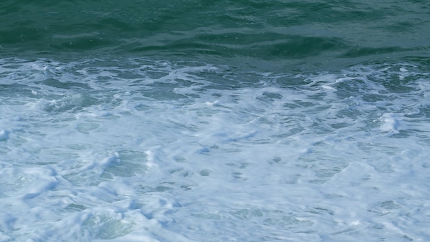 Le onde dell'oceano si scontrano e schiumano onde turchesi con schiuma bianca al rallentatore
