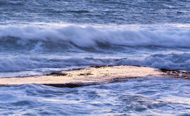 Le onde dell'oceano spruzzano sulla calma piattaforma rocciosa all'alba