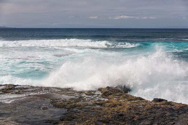 Le onde dell'oceano turbolente con schiuma bianca battono le pietre costiere