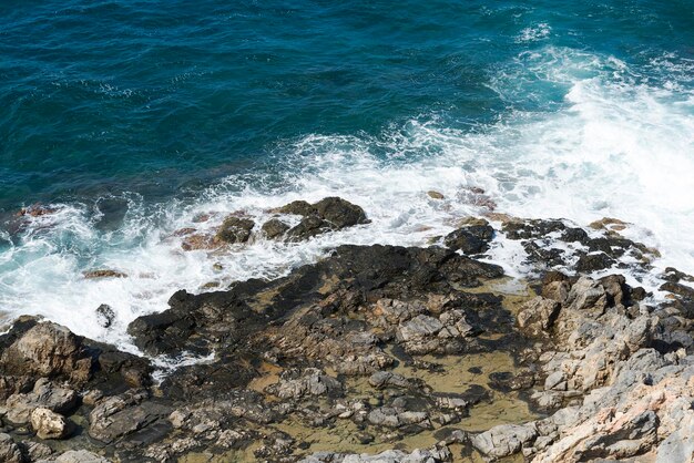 Le onde si infrangono sulla spiaggia rocciosa formando spruzzi Onde e spruzzi sulla spiaggia