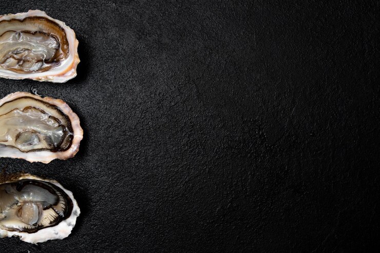 Le ostriche aperte fresche della prelibatezza del mare sono disposte su uno sfondo scuro