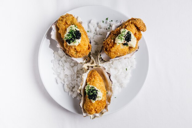 Le ostriche fritte nel grasso bollente che completano con maionese e caviale sono servito in piatto bianco.