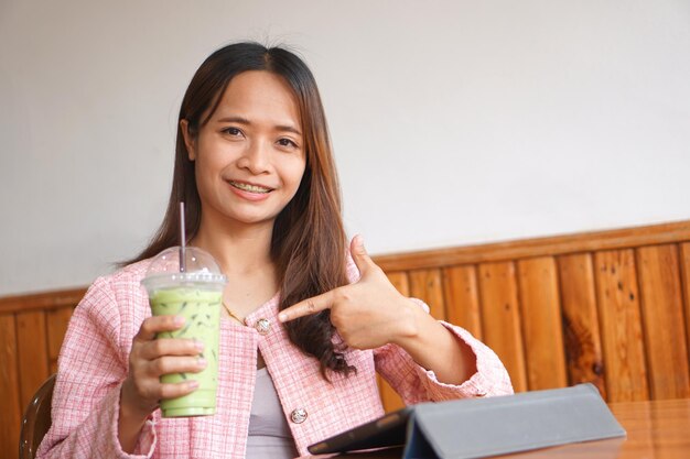 Le parentesi graffe della donna asiatica guardano il computer Bevono il tè verde per rinfrescarsi