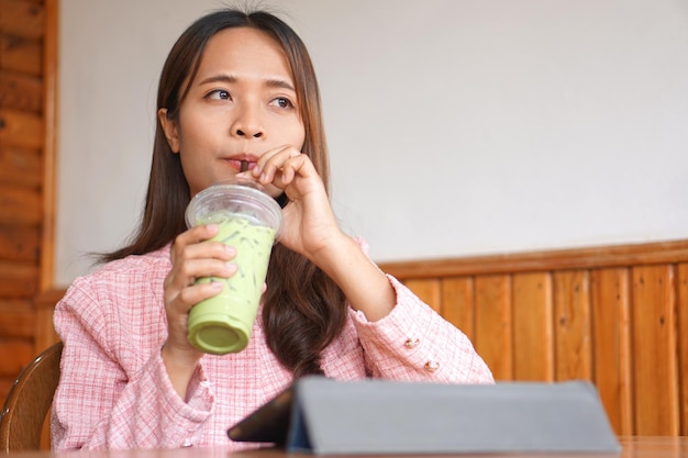 Le parentesi graffe della donna asiatica guardano il computer Bevono il tè verde per rinfrescarsi