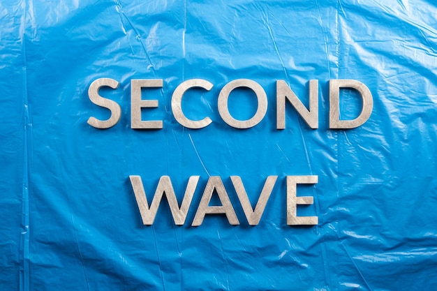 Le parole seconda ondata posate con lettere di metallo argentato su uno sfondo di pellicola di plastica blu stropicciata