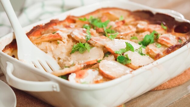 Le patate al forno appena sfornate guarnire con prezzemolo in una teglia di ceramica bianca.