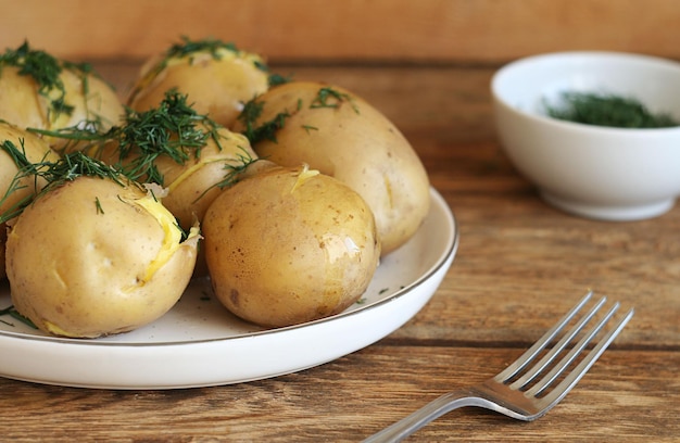 Le patate bollite giacciono in un piatto bianco su un tavolo di legno Concetto di cibo agricolo