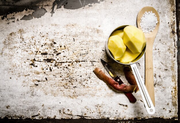 Le patate sbucciate in una casseruola di metallo con un cucchiaio di sale alla rustica