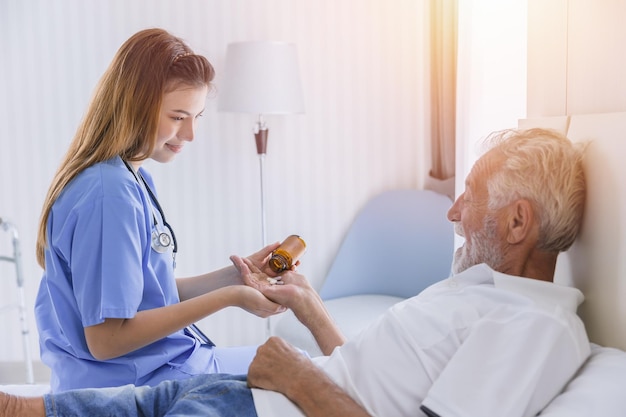 Le persone anziane dell'uomo anziano si sdraiano sul letto l'assistenza sanitaria dando pillole medicinali dall'infermiera all'assistenza domiciliare