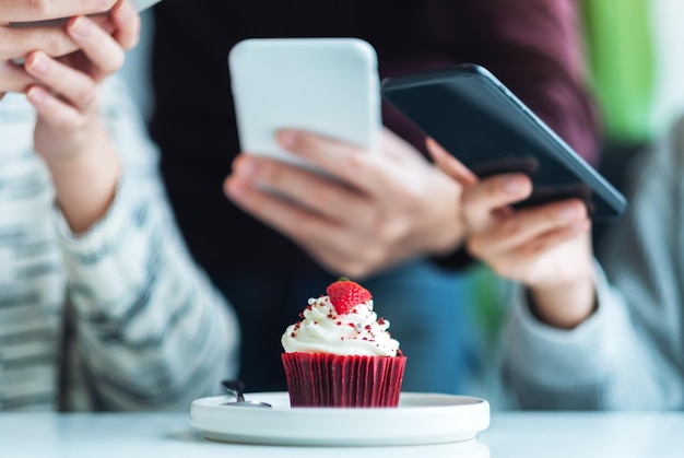 Le persone che usano il telefono cellulare per scattare una foto di un cupcake prima di mangiare al bar