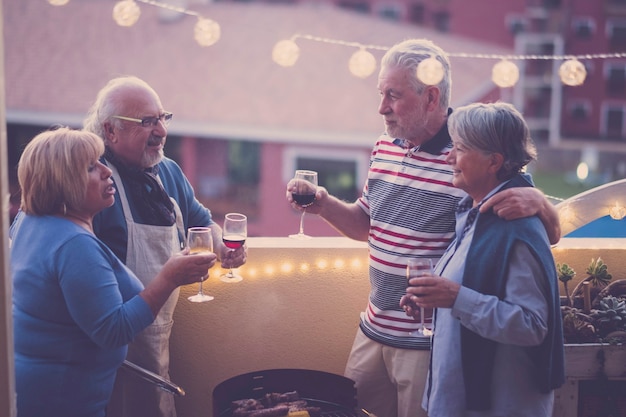 Le persone degli amici notturni festeggiano insieme al vino rosso e bianco divertendosi insieme - vista sulla città sulla terrazza - barbecue e amicizia per uomini e donne adulti anziani - coppie mature caucasiche
