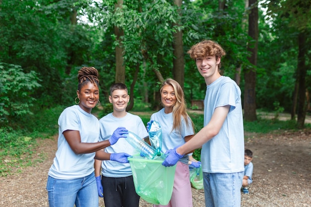 Le persone felici del servizio comunitario che puliscono il parco locale hanno un sacchetto della spazzatura e lo stanno riempiendo con la spezzatura che hanno trovato nel parco. Sono due inginocchiati e altri dietro di loro.