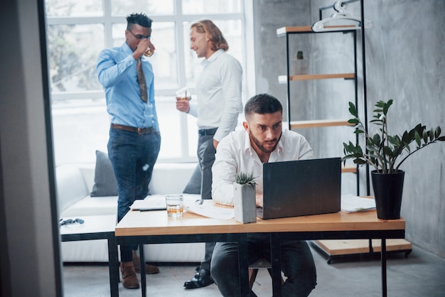 Le persone hanno un'enfasi sullo sfondo. Il giovane uomo d'affari si siede sulla sedia davanti al computer portatile e lavora con i rapporti