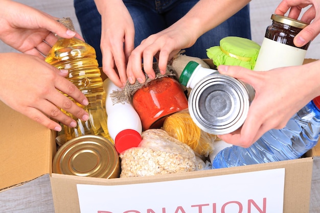 Le persone producono alimenti dalla scatola delle donazioni su sfondo grigio