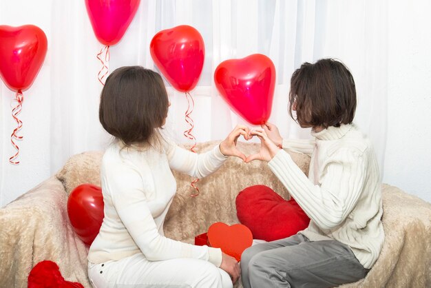 Le persone si tengono le mani insieme con un simbolo di cuore tra i palloncini a forma di cuore amante di San Valentino