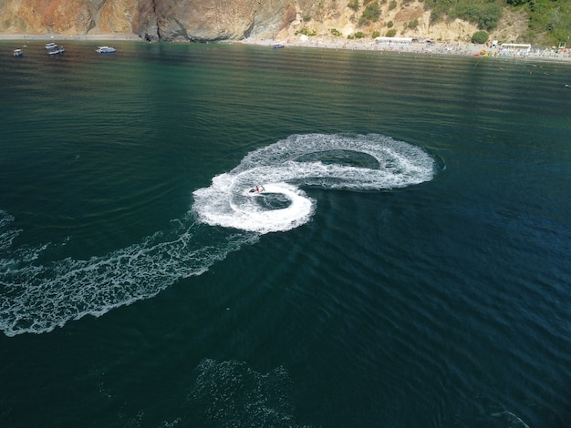 Le persone stanno giocando a una moto d'acqua nel mare lasciando impronte bianche astratte sulla parte superiore dell'antenna dell'acqua